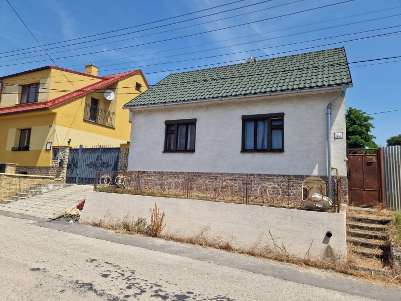 Rodinný dům ve Štefanově s bílou omítkou a zelenou střechou na tiché ulici.