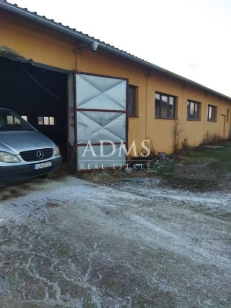 Obrázek z Ladiec zobrazuje sklady a haly s automobilem u otevřené brány.