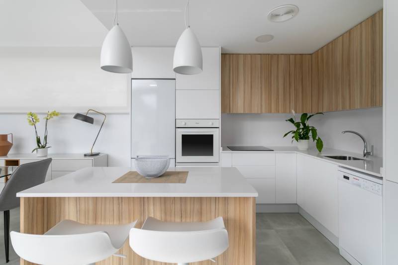 Kuchyně ve vile s bílými a dřevěnými skříňkami, osvětlená moderními lampami.