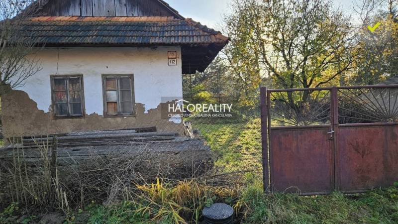 Starší dům s poškozenou fasádou a dřevěnou střechou, obklopený zelenými pozemky k bydlení.