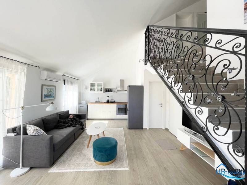 Obývací prostor v rekreačním apartmánu s kuchyní, sedačkou a schodištěm.
