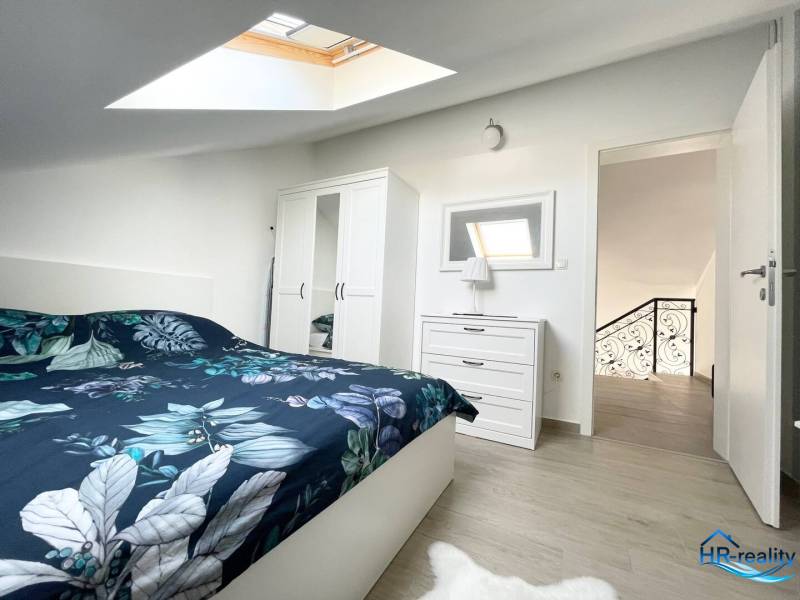 Ložnice v rekreačním apartmánu s postelí, skříní a střešním oknem.