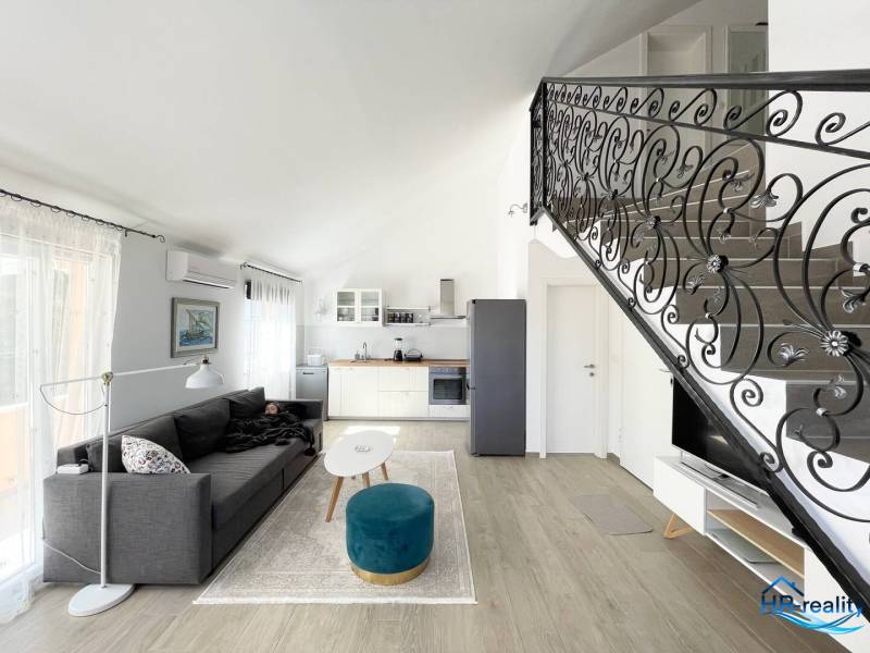Obývací pokoj s pohovkou, kuchyňským koutem a ozdobným zábradlím, v rekreačním apartmánu.