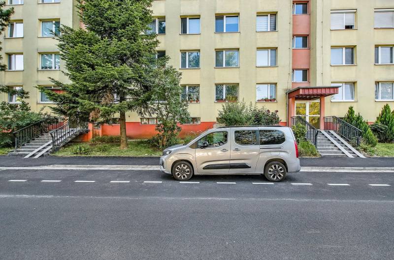 Ulice Landauova v Bratislavě-Dúbravce s obytnou budovou a zaparkovaným autem před ní.