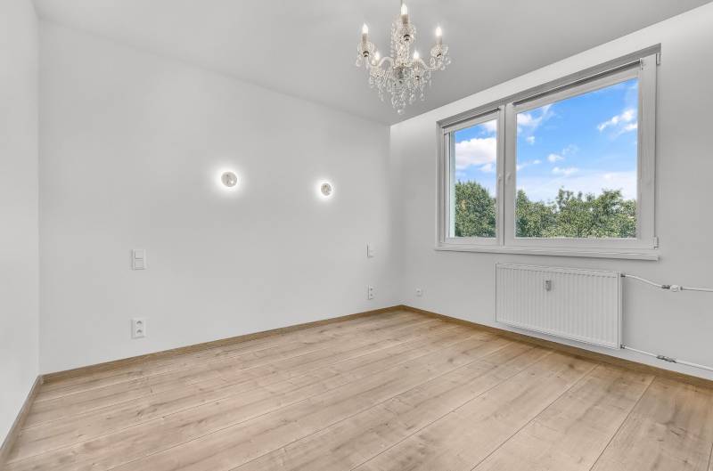 Prázdný pokoj s dřevěnou podlahou, lustrem a velkým oknem, 4pokojový byt.