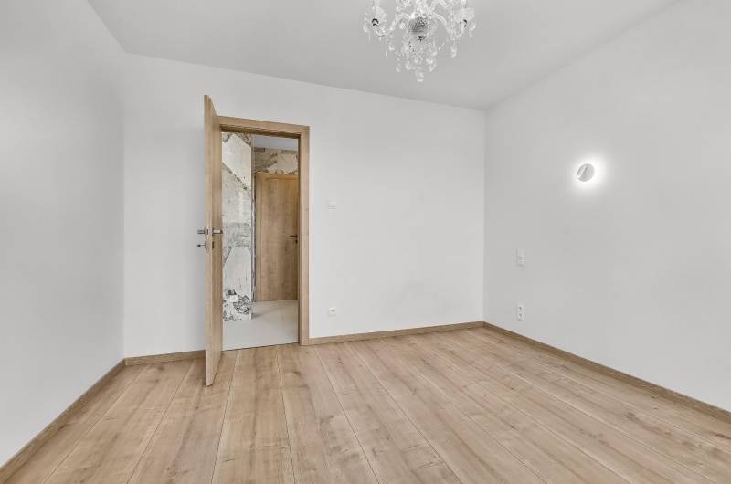 Prázdný pokoj s dřevěnou podlahou a lustrem ve 4pokojovém bytě.