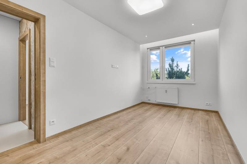 Prázdná místnost s dřevěnou podlahou a plastovým oknem ve 4-pokojovém bytě.