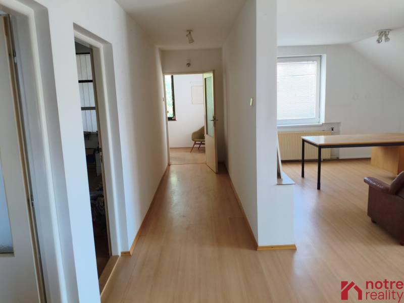 Chodba s dřevěnou podlahou, vlevo místnosti, vpravo pokoj se stolem v rodinném domě.