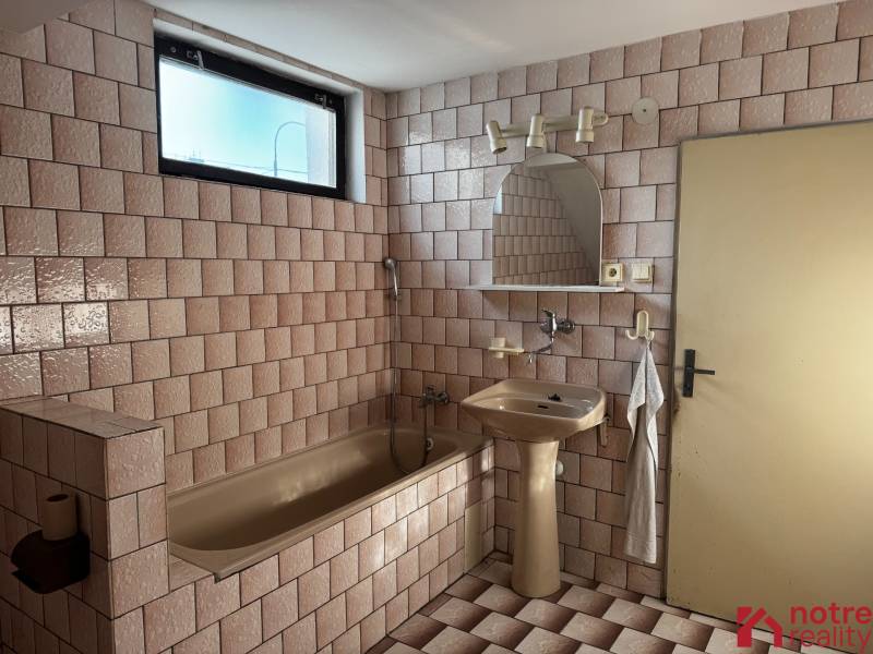 Koupelna rodinného domu s vanou a umyvadlem, obložená dlaždičkami.