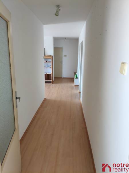 Chodba s dřevěnou podlahou a bílými stěnami vedoucí ke dveřím v rodinném domě.