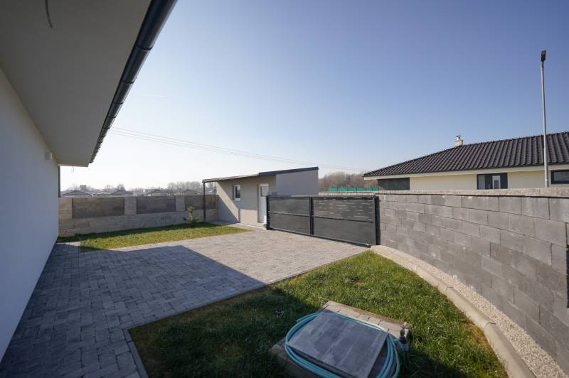 Dvůr rodinného domu na Nevädzové ulici v Kalinkově s trávníkem a zámkovou dlažbou.