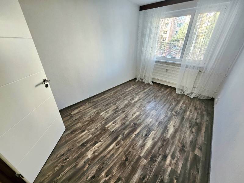 Prázdný pokoj s laminátovou podlahou a velkým oknem ve 3-pokojovém bytě.