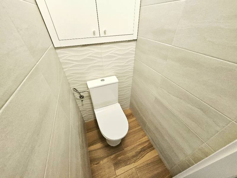 Toaleta v 3-pokojovém bytě s dřevěnou podlahou a jemnými obklady stěn.