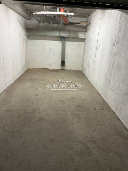 Uzavřený prostor garáže s betonovou podlahou a bílými stěnami, číslo 19, potrubí na stropě.