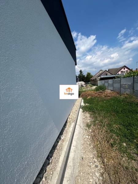 Stěna rodinného domu v Žihárci s přilehlým pozemkem pod modrou oblohou.