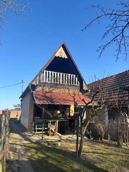 Chata se šikmou střechou a verandou, obklopená zahradními rekreačními pozemky.