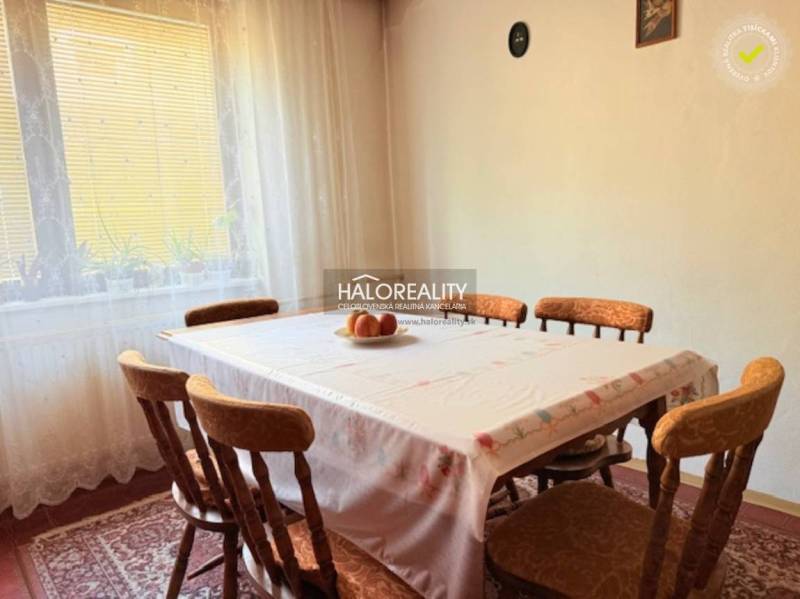 Jídelna s dřevěným stolem a židlemi, zdobená záclonami a obrazem s příbory.