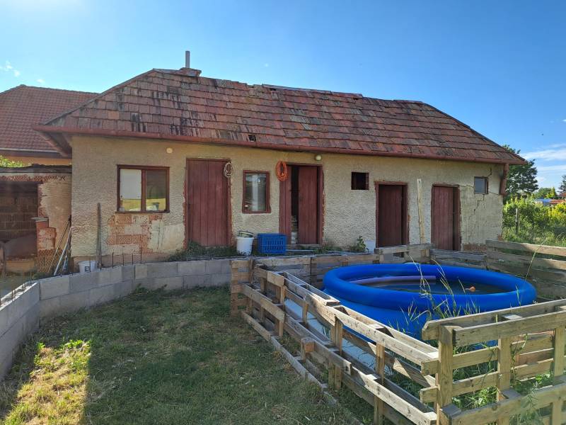 Rodinný dům v Kmeťově s přístavbou, nafukovací bazén a jednoduchý dřevěný plot.