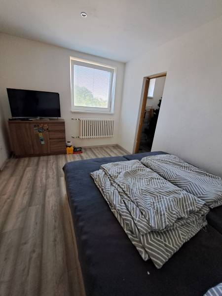 Pokoj v rodinném domě s televizí, pohovkou a oknem přinášejícím přirozené světlo.