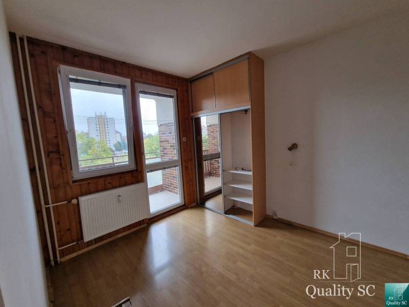 Prázdný pokoj ve čtyřpokojovém bytě s dřevěnými panely a výhledem na balkon.