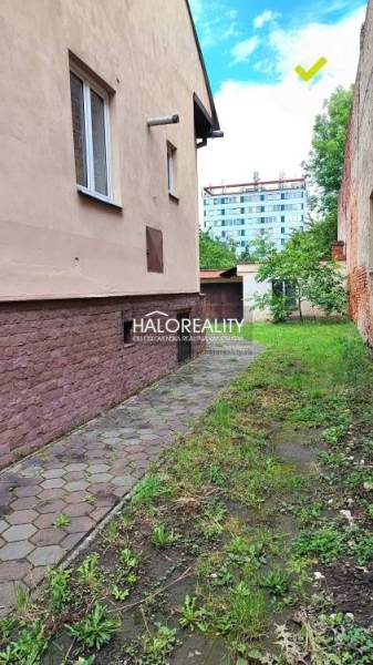 Úzký chodník u rodinného domu v Lučenci s trávou a zelení.