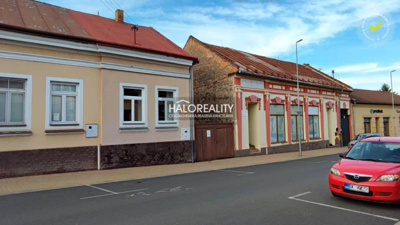 Rodinný dům v Lučenci se staršími fasádami a zaparkovaným červeným autem na ulici.
