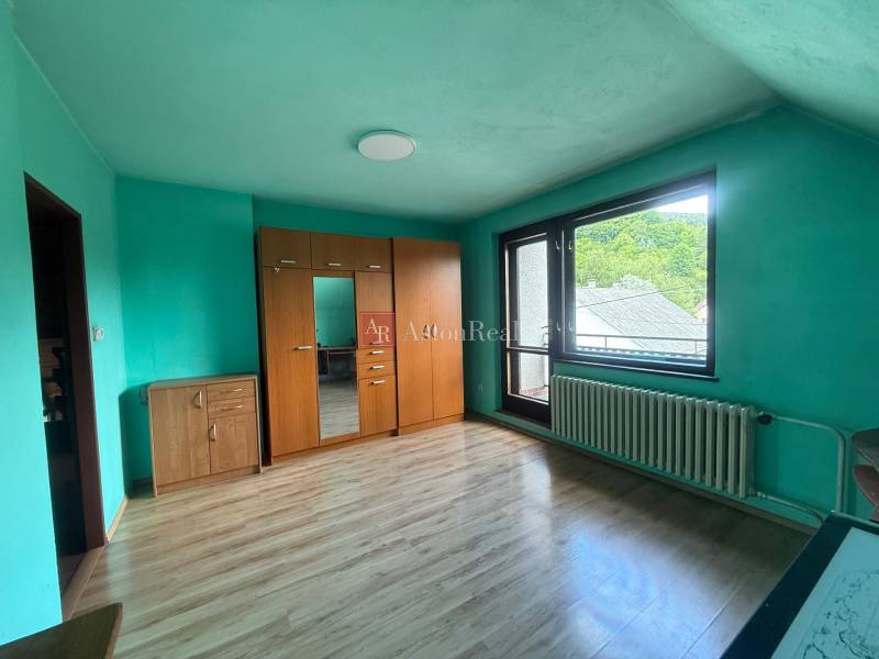 Pokoj v rodinném domě s dřevěnou podlahou, šatní skříní a balkónovým oknem.