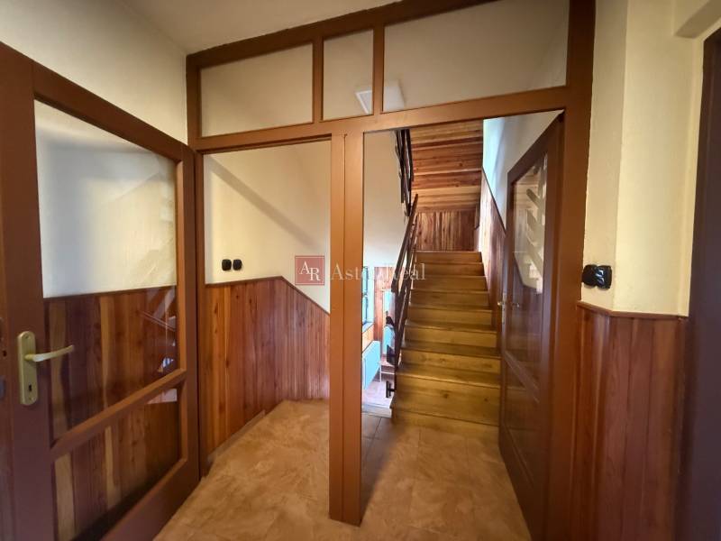 Dřevěné schodiště a dveře v rodinném domě s obloženými stěnami a dlažbou.