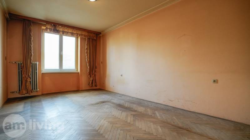 Pokoj v 2pokojovém bytě s dřevěnou podlahou a velkým oknem.