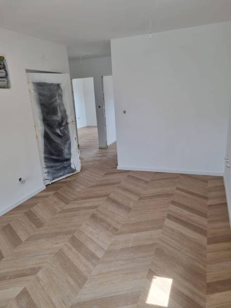 Neúplně dokončený prostor ve 4-pokojovém bytě s položenou dřevěnou podlahou.