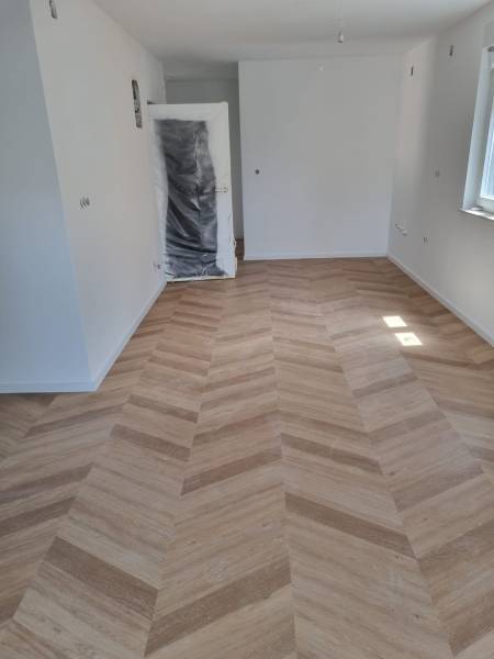 Interiér 4-pokojového bytu s novou dřevěnou podlahou a osvětlením z okna.