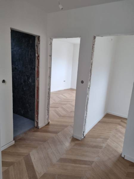 Chodba ve 4pokojovém bytě s dřevěnou podlahou a otevřenými dveřmi.