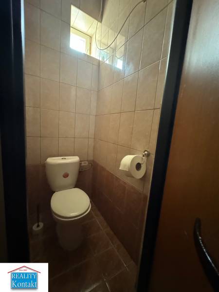 Toaleta s obloženými stěnami v obchodních prostorách, s oknem pro přirozené světlo.