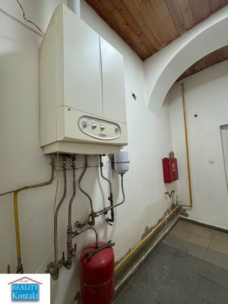 Kotel a potrubí v obchodních prostorách, stěna s mírnými stopami opotřebení.