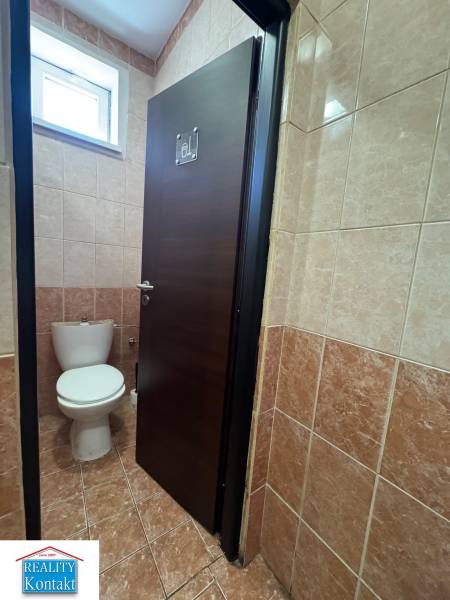 Toaleta se zavřenými dveřmi v obchodních prostorách, obložená hnědými dlaždicemi.