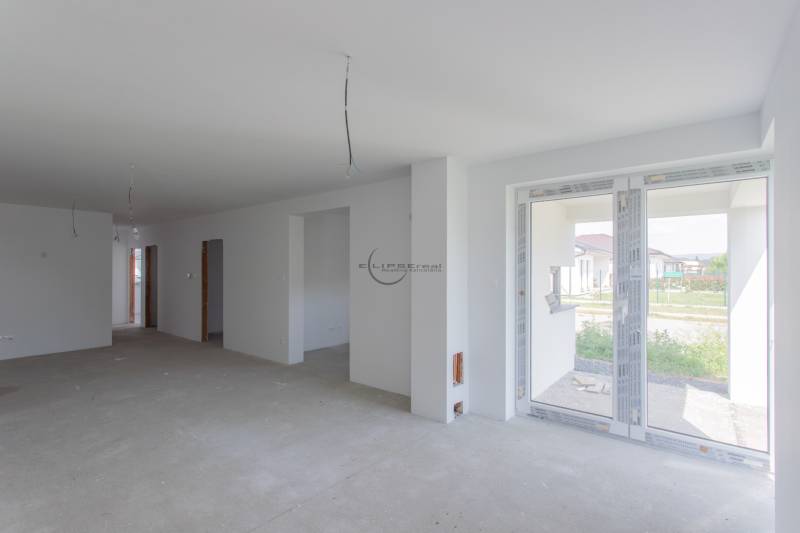 Interiér rodinného domu s nedokončenou podlahou a velkými okny.