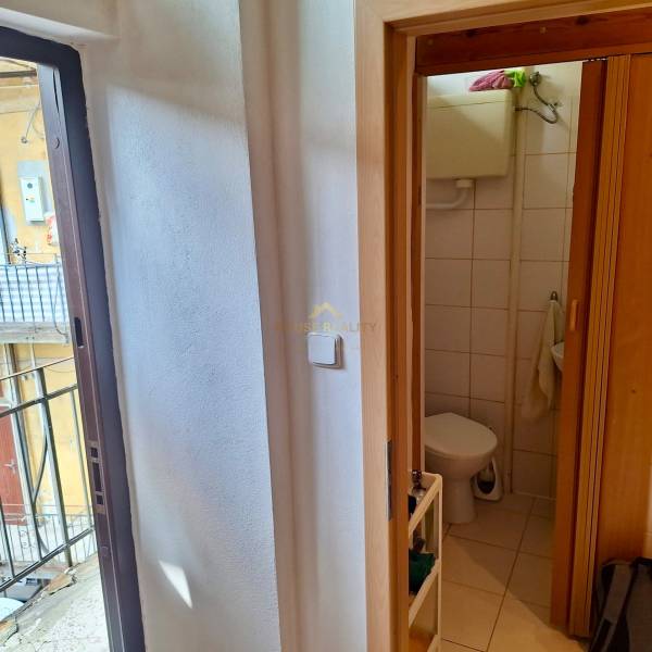 V 1-pokojovém bytě je vidět koupelna s toaletou a dveře vedoucí na balkon.