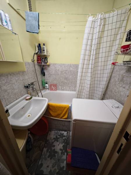 Koupelna v 2-pokojovém bytě s pračkou, vanou, umyvadlem a světlými obklady.