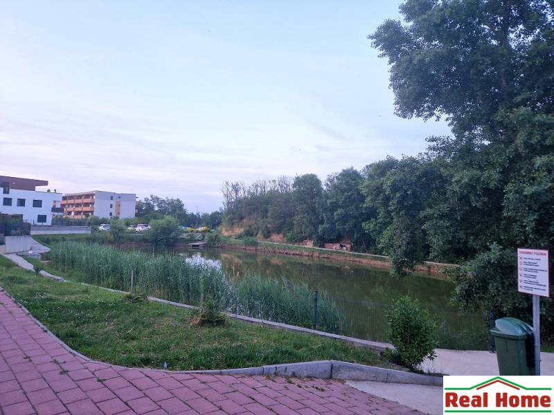 Jezero s chodníkem v Senci, ulice Vtáčí, mezi stromy a obytnými budovami.