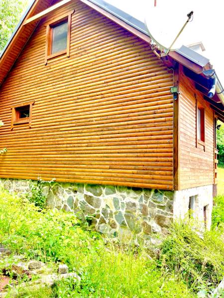 Dřevěný rodinný dům ve Štefultově s kamennou základnou obklopený zelení.