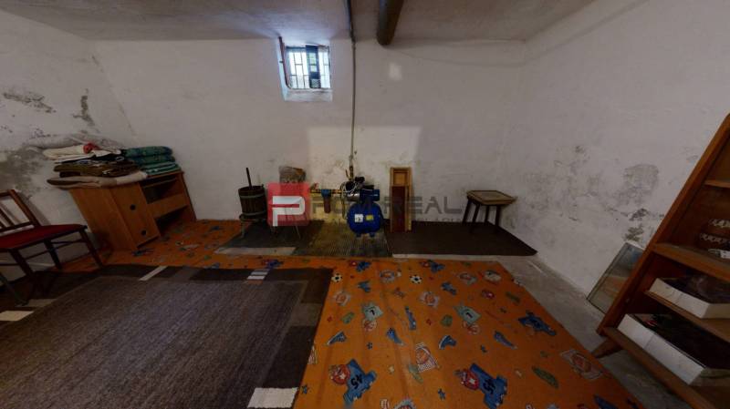 Suterén rodinného domu s malým oknem, koberec a vnitřní zařízení včetně křesla.