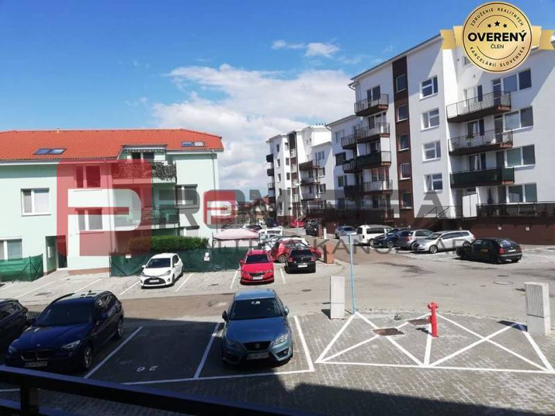Parkoviště na ulici Slavomírova s auty před budovami v městském prostředí.