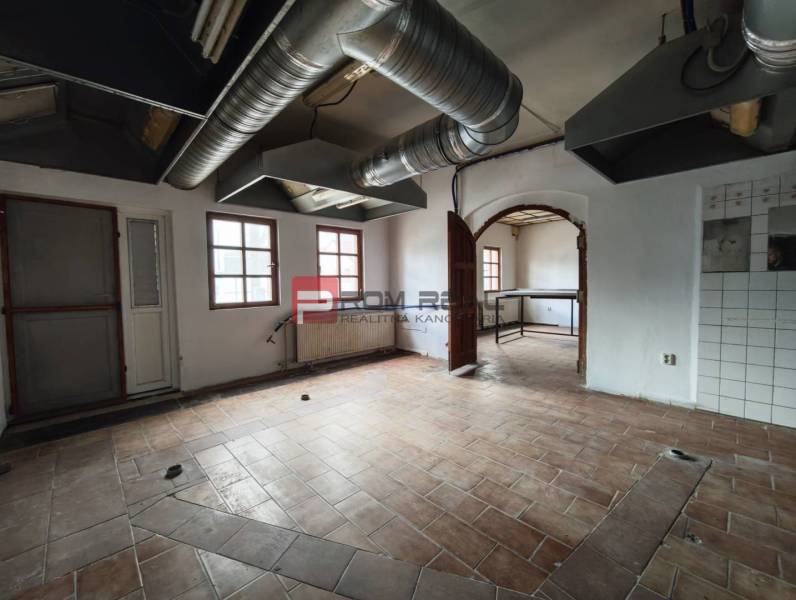 Prostor s dlažbou a ventilačními trubkami, vhodný pro obchodní prostory.