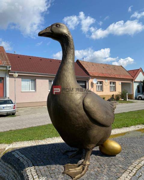 Socha husy se pozlaceným vejcem, na ulici Slovenský Grob, v pozadí jsou sklady a haly.