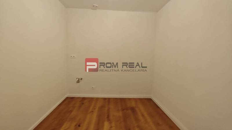 Pokoj s bílými stěnami a dřevěnou podlahou ve 4pokojovém bytě.