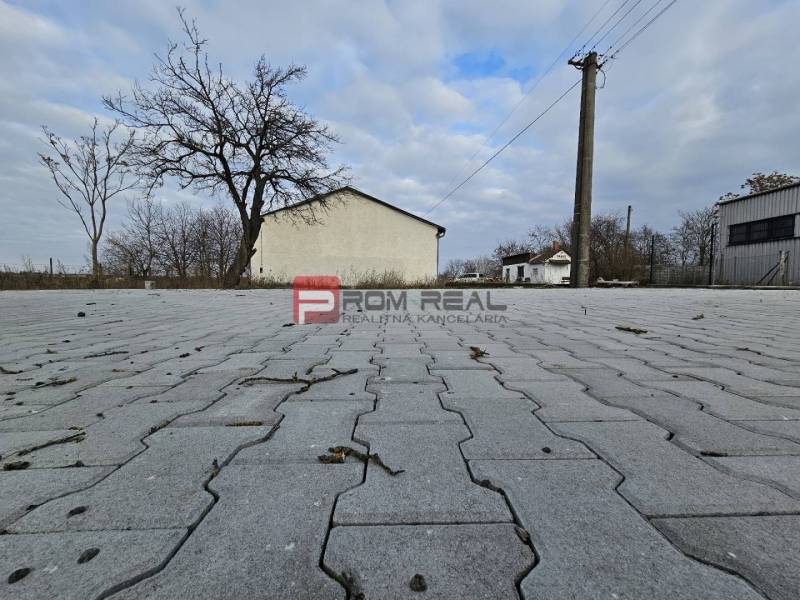 Povrch na ulici Partizánska, vedle sklady a haly, s holými stromy.