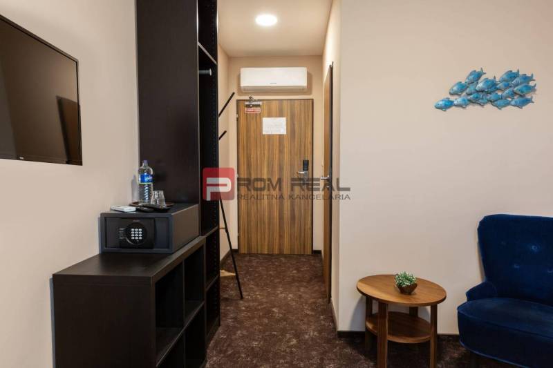 Pokoj v hotelu s nábytkem, trezorem a televizí, dekorace na stěně.