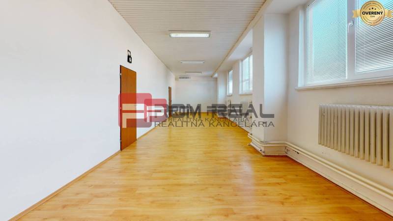 Prostorná světlá místnost s dřevěnou podlahou, radiátory a okny ve skladech a halách.