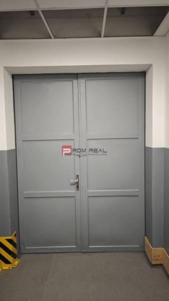Šedá kovová dvoukřídlá brána ve skladech a halách.