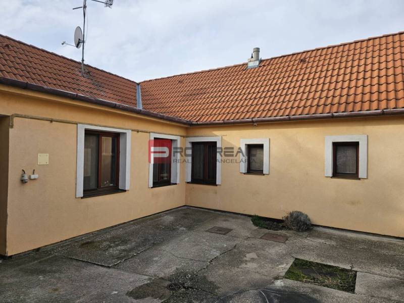 Dvůr rodinného domu na Sluneční ulici v Pezinku s betonovou dlažbou a oranžovou fasádou.